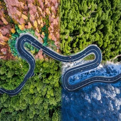 Winding asphalt road through diverse weather conditions, illustrating all-weather application of cold mix asphalt