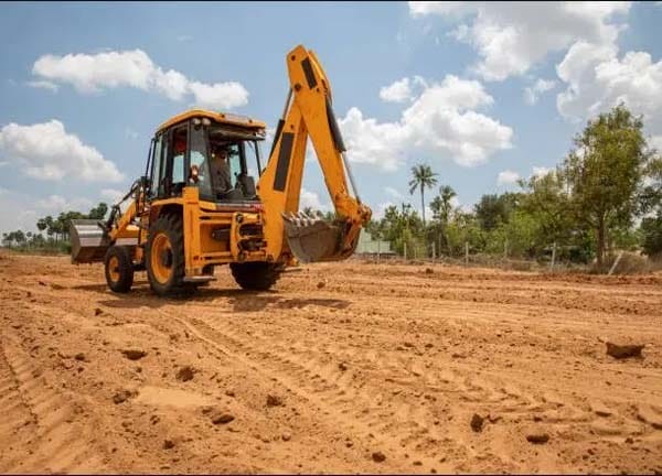 Excavator moving soil on a large, cleared plot of land during the early stages of road construction.