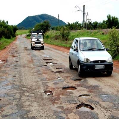 Severely damaged rural road with multiple potholes caused by heavy traffic loads