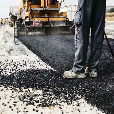 Asphalt paving in progress with visible material quality issues due to use of inferior construction materials