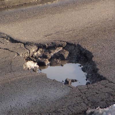 Large pothole filled with water on deteriorated road due to lack of preventative maintenance