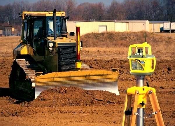 “Bulldozer clearing and leveling ground at a construction site with surveying equipment in the foreground.