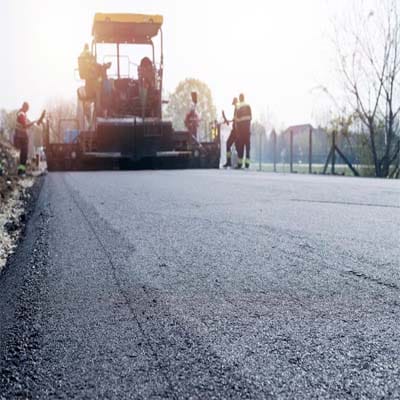 Road crew applying cold mix asphalt on a rural road, highlighting its versatile applications across different environments