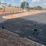 Vibrant orange road roller compacting freshly laid asphalt on a rural road project under clear skies